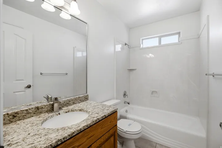 Bathroom featuring a granite-finish countertop, wood-finish vanity, large mirror, and an integrated tub and shower unit with a transom window