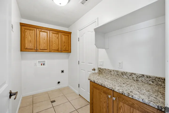 Laundry area featuring a built-in granite-finish countertop, wood-finish cabinetry, tile flooring, and integrated wall shelving