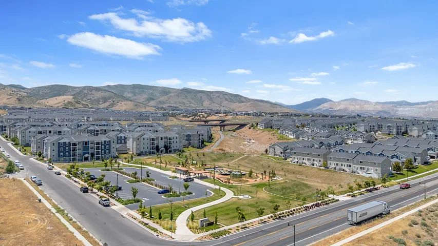 Expansive community featuring multi-story residential buildings and townhomes, a manicured green space with walking paths, and a substantial parking area