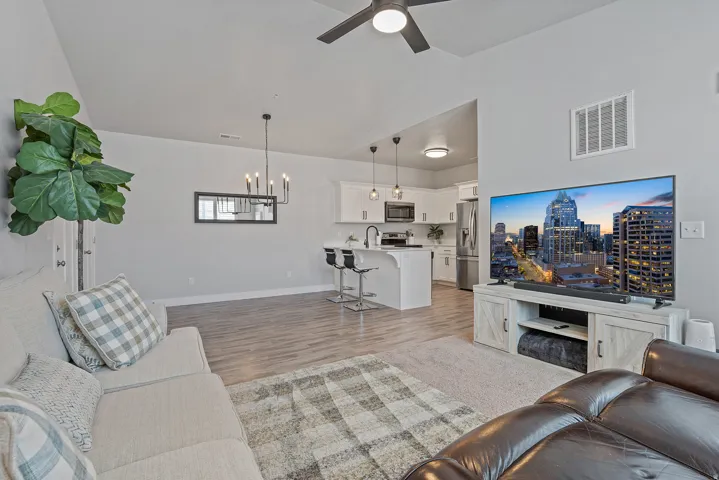 Open-concept living area featuring wood-finish flooring, a contemporary ceiling fan, and a kitchen with white cabinetry and stainless steel appliances