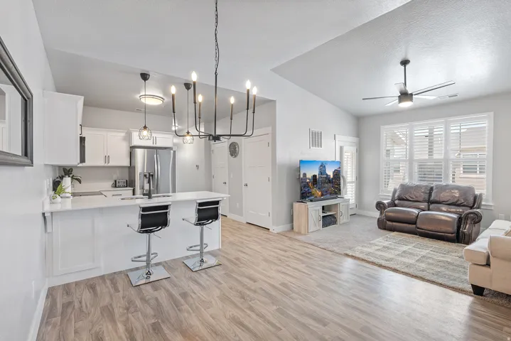 Open-concept living area featuring wood-finish flooring, a contemporary kitchen island with seating, stainless steel appliances, a modern chandelier, and recessed lighting