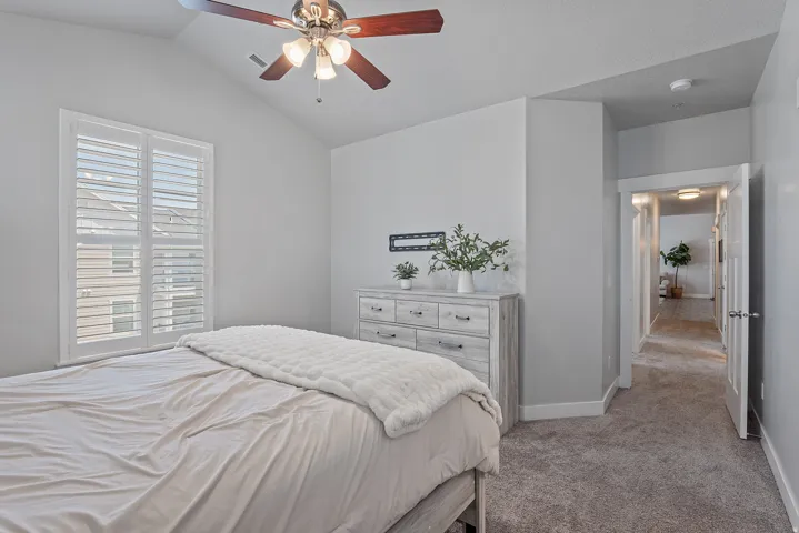Carpeted bedroom featuring vaulted ceilings, a ceiling fan with light, white plantation shutters, and a white six-drawer dresser