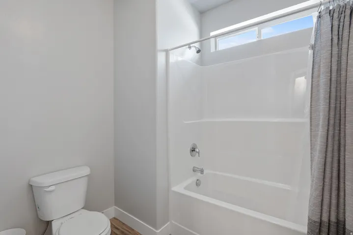 Bathroom featuring a white toilet, light gray walls, and wood-finish flooring
