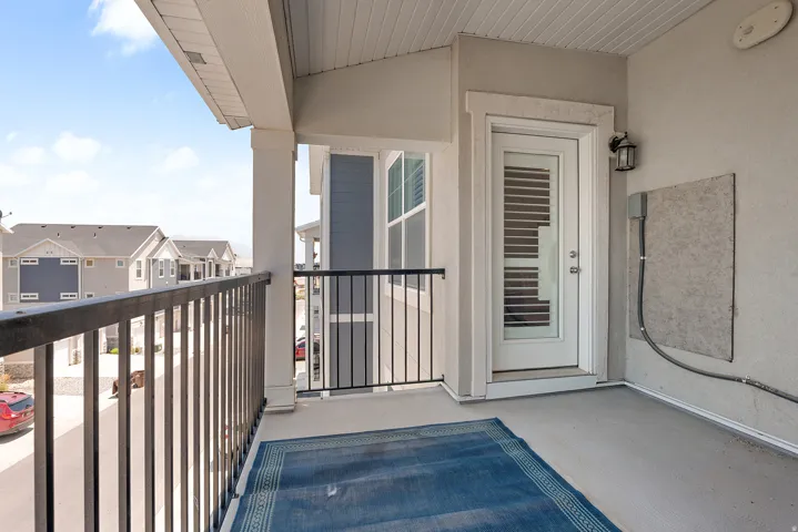 Exterior balcony featuring a concrete floor, black metal railings, and a white paneled door with louvered glass