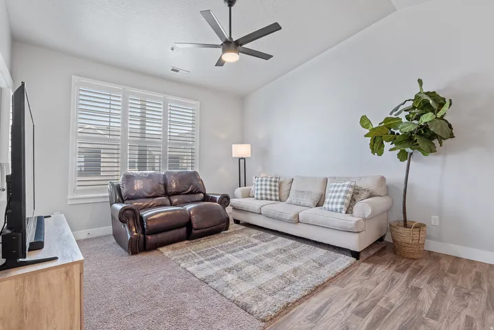 Living area featuring vaulted ceilings, a ceiling fan, and large windows with privacy blinds