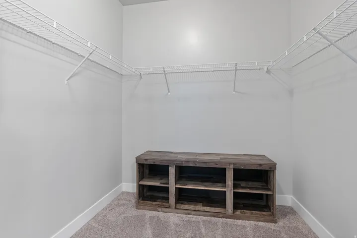 Spacious walk-in closet featuring wire shelving, neutral carpeting, light gray walls, white baseboards, and a built-in wood-finish storage unit with open shelving