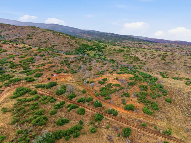 Expansive mountainous terrain featuring natural vegetation, a winding dirt road, and a distant small structure