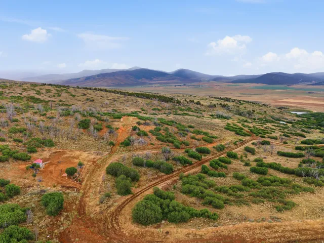 Expansive undeveloped land featuring rolling hills, scattered green shrubbery, and distant mountainous terrain