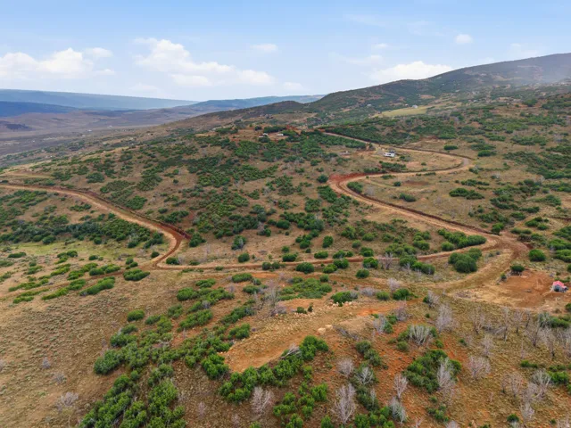 Expansive hillside acreage featuring a winding dirt road and scattered green shrubbery, with distant mountains forming a natural backdrop