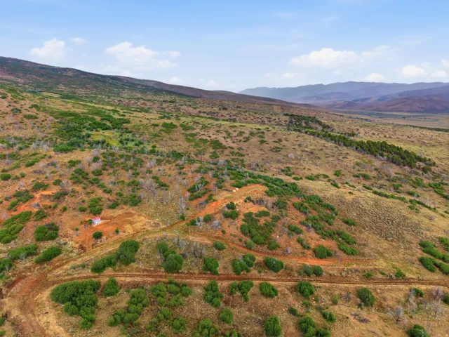 Expansive rural landscape featuring a single-story structure with a red roof, surrounded by varied vegetation and natural terrain