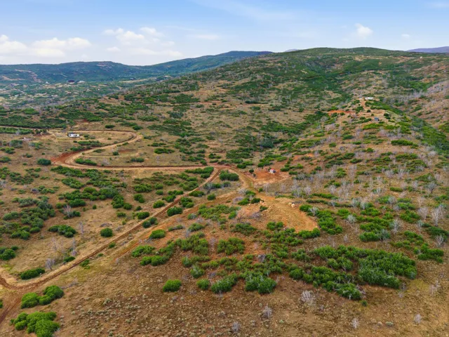 Expansive hillside property featuring established dirt roads, varied natural vegetation, and distant mountain ranges