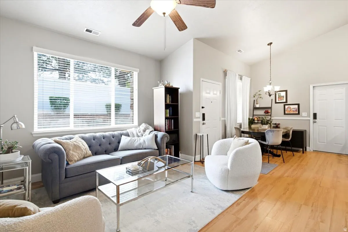 Open-concept living and dining area featuring wood-finish flooring, vaulted ceilings, a ceiling fan, and large windows with blinds