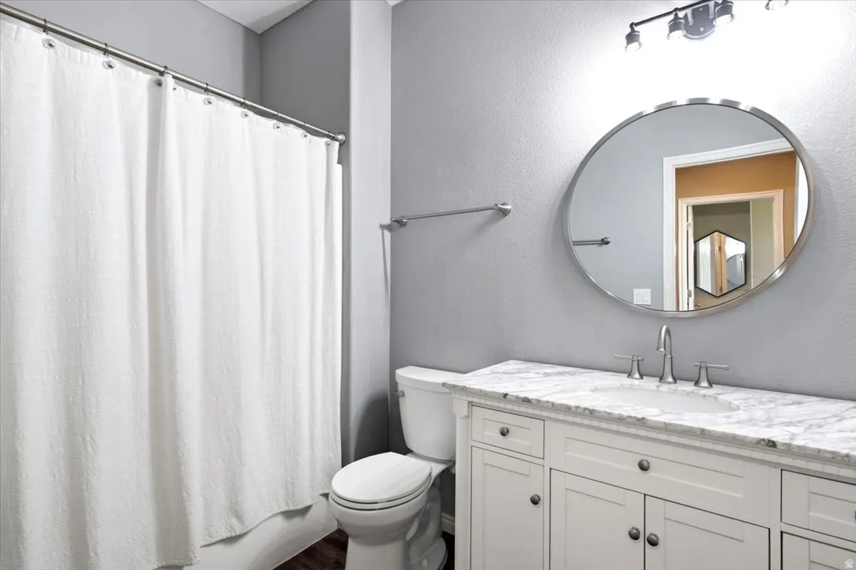 Bathroom featuring a white vanity with panel cabinetry, a stone countertop, an undermount sink, and a circular mirror