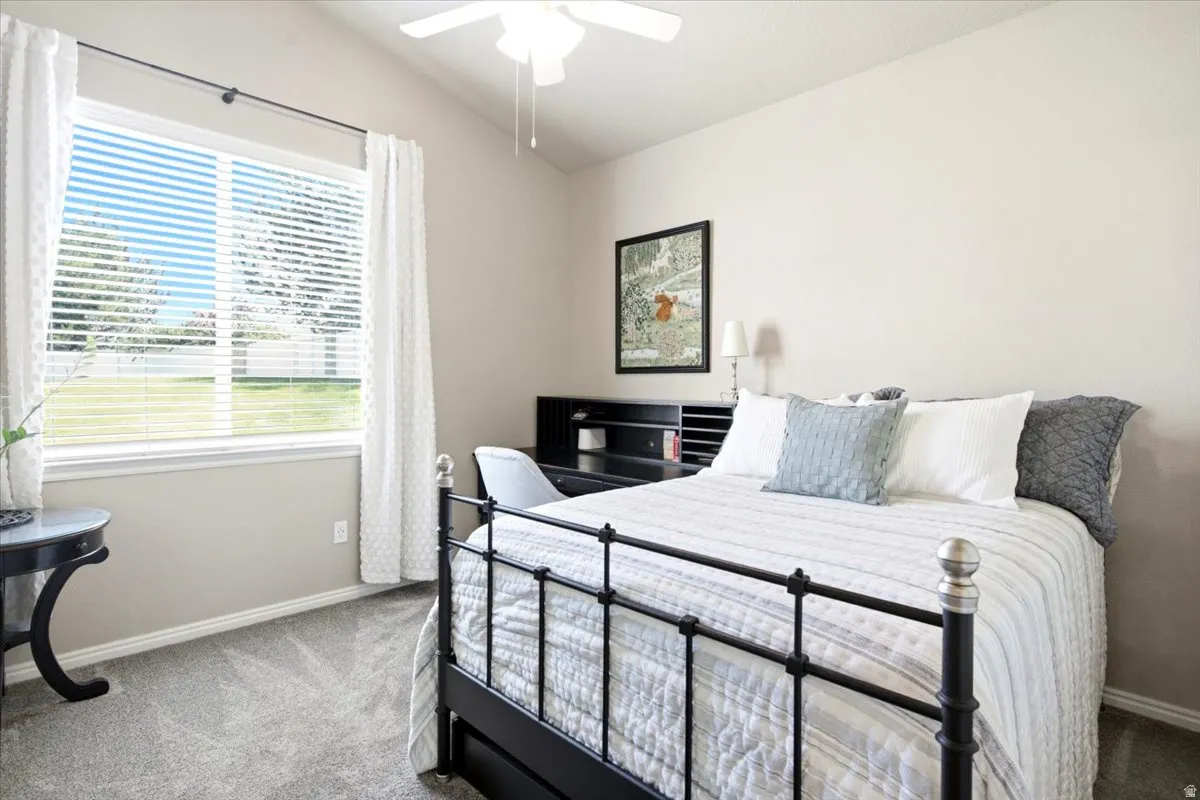 Spacious room featuring vaulted ceilings, a large window, light gray carpet, and a ceiling fan