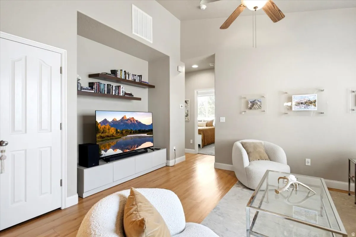 Living area featuring vaulted ceilings, wood-finish flooring, a built-in media niche with floating shelves, and a ceiling fan with light fixture