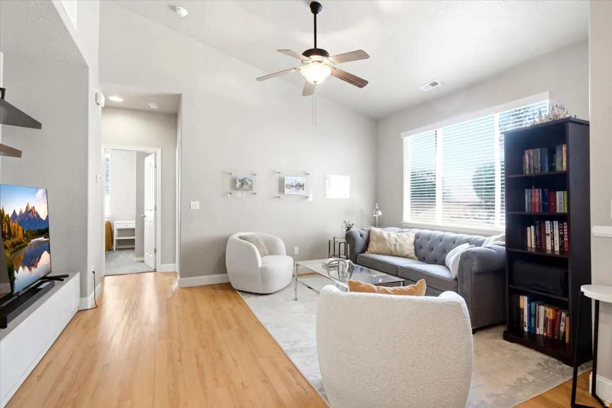 Vaulted ceiling living area featuring light wood-finish flooring and a central ceiling fan