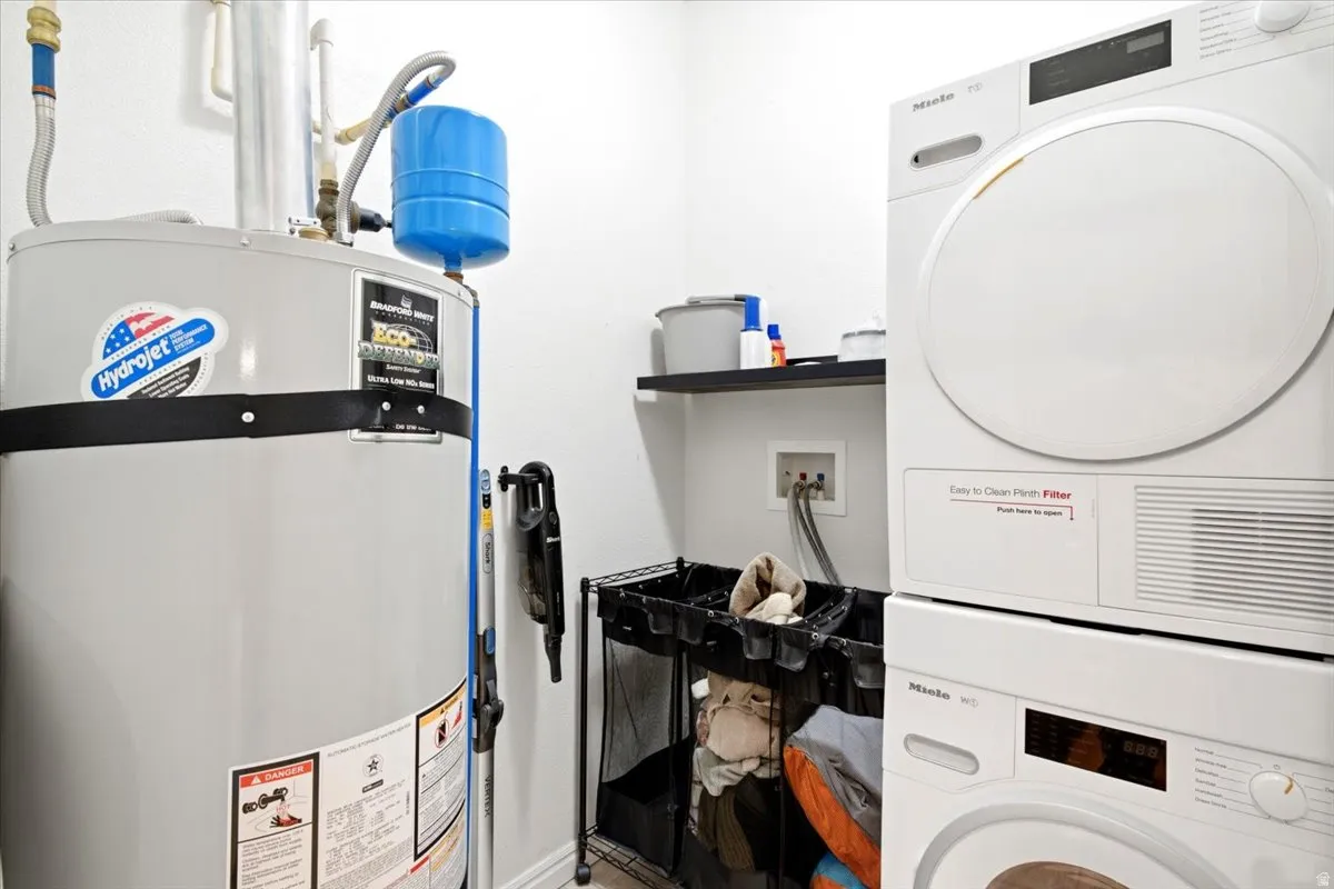 Dedicated utility area featuring a water heater, stacked washer and dryer, and wall-mounted shelving