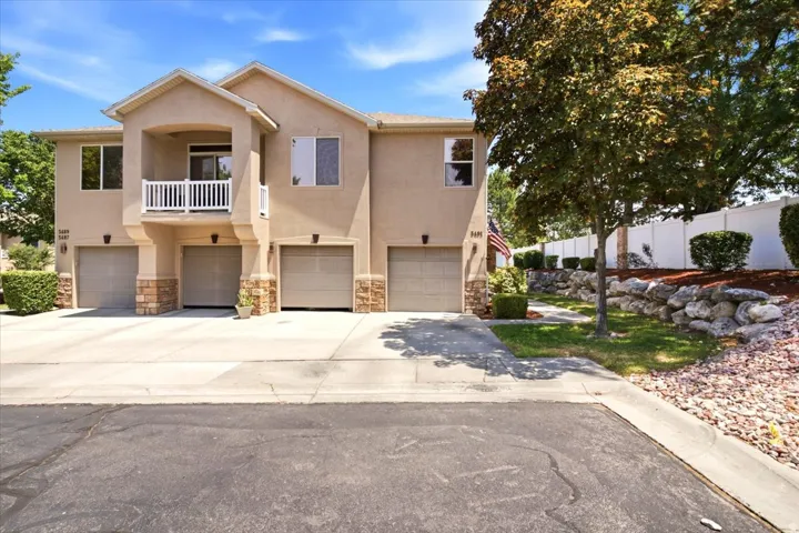 Multi-level stucco exterior featuring stone accents, individual garage doors, and a second-story balcony with white railing