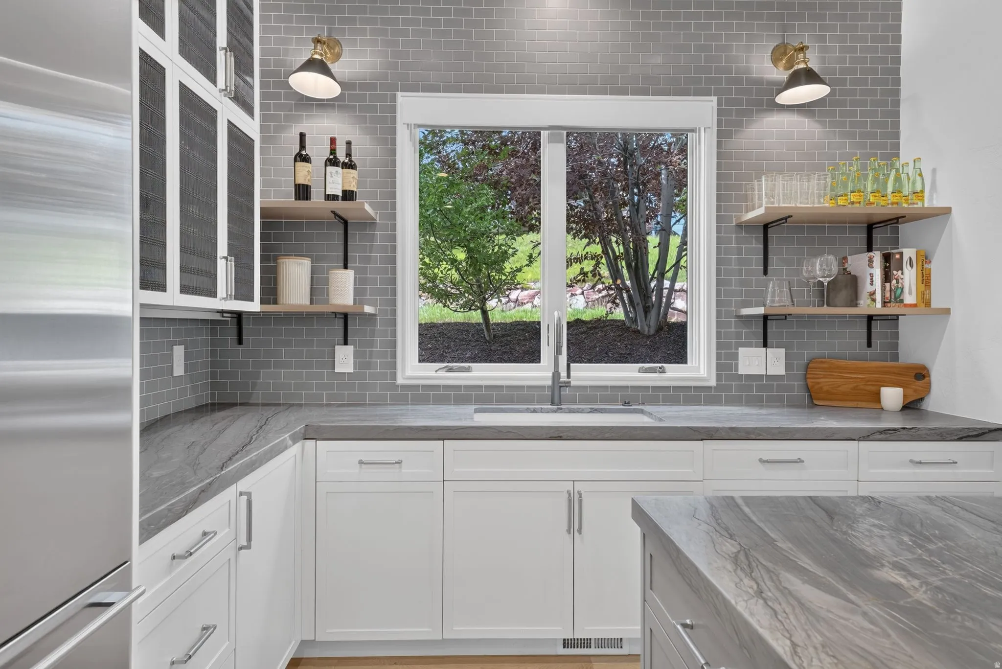 Kitchen with grey subway tile backsplash, white shaker cabinetry, stainless steel sink, and light wood-finish open shelving