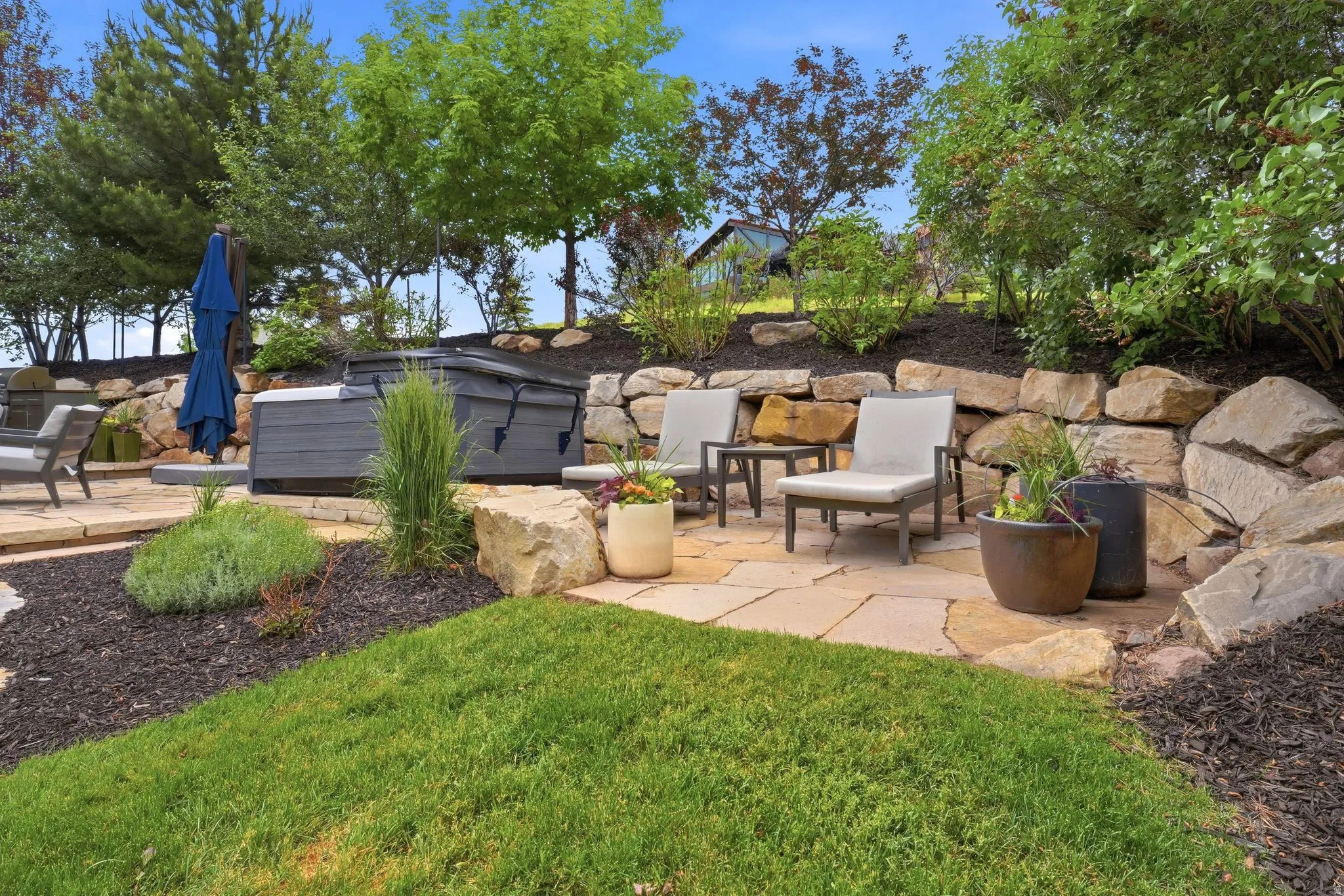 Flagstone patio area featuring a built-in hot tub, natural rock retaining wall, and mature landscaping