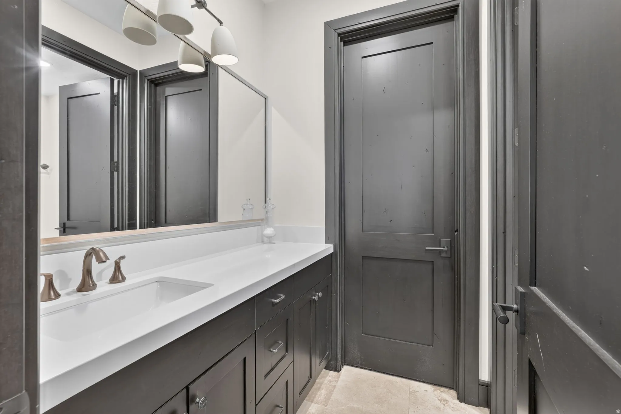 Bathroom vanity featuring a single integrated sink, white countertop, dark wood-finish cabinetry, and brushed bronze fixtures