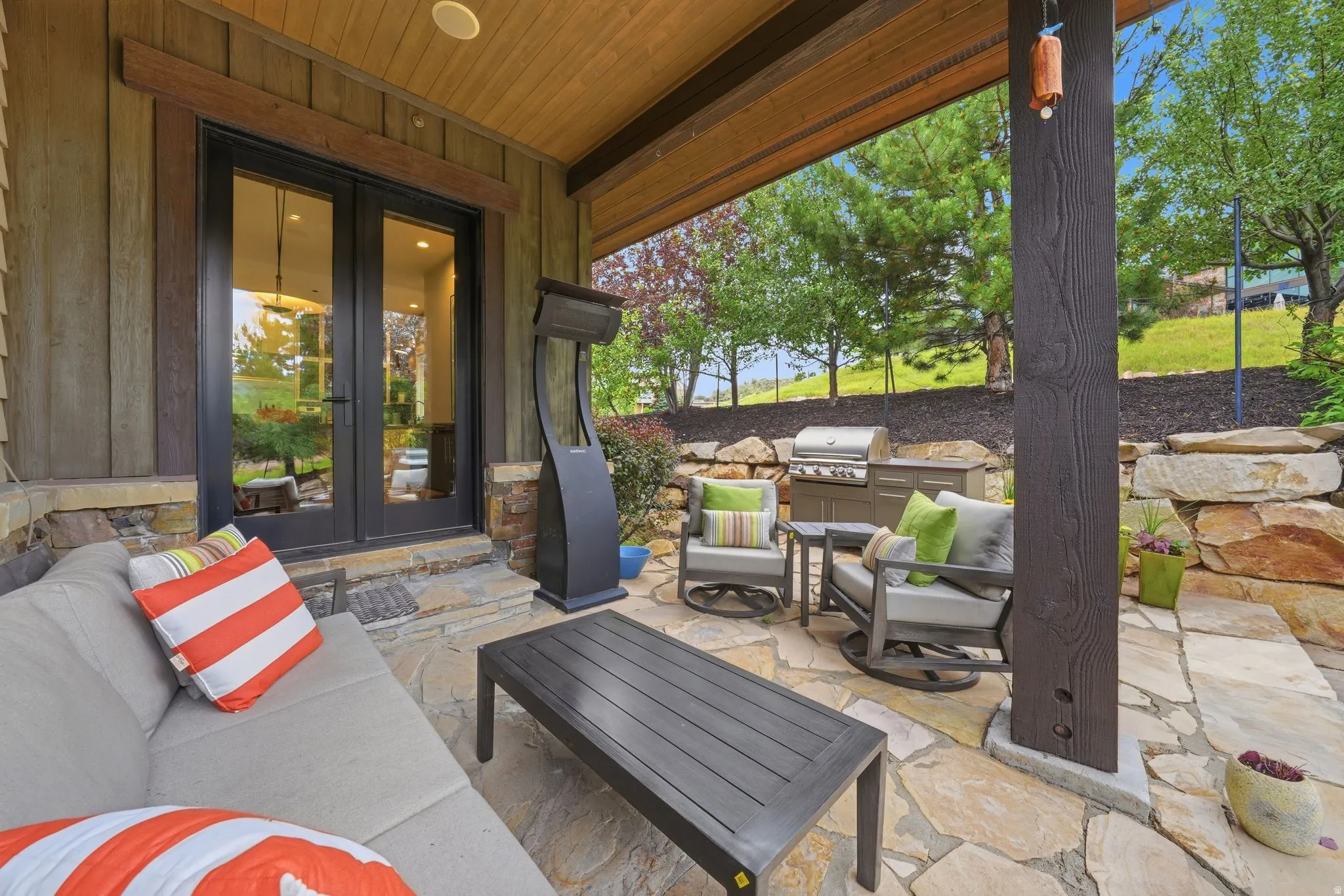 Covered patio featuring flagstone flooring, a built-in outdoor kitchen with a grill, and substantial stone retaining walls