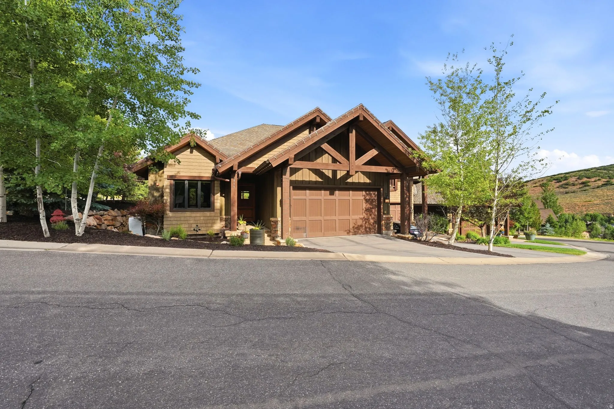 Mountain-style exterior featuring a prominent two-car garage, exposed wood beams, and natural wood siding