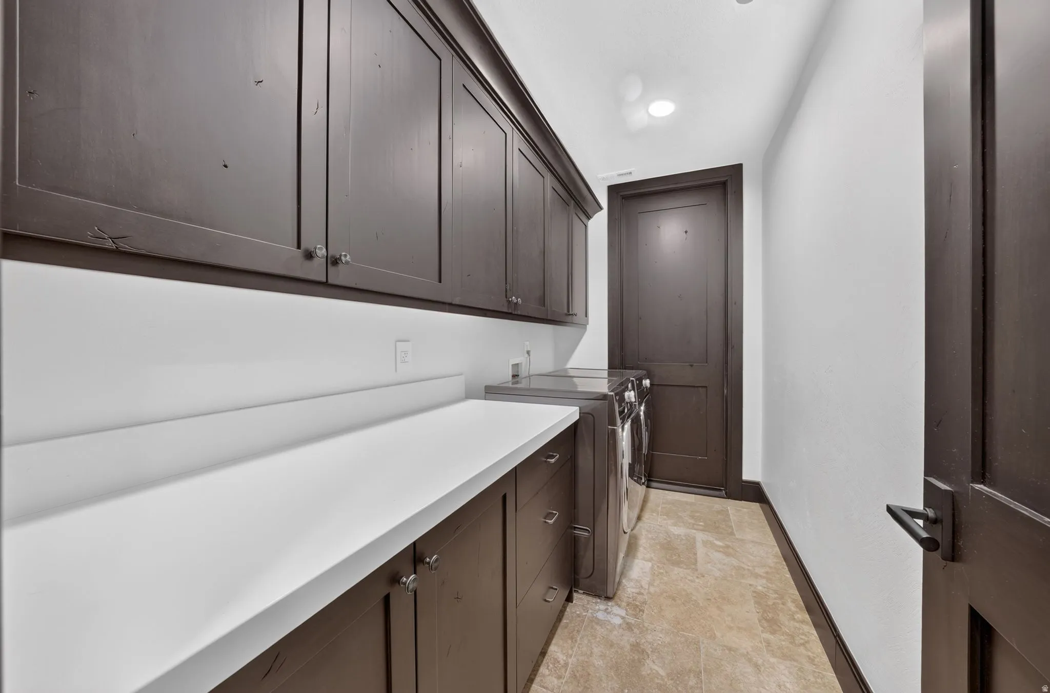 Laundry area featuring extensive dark wood cabinetry, white countertops, under-cabinet lighting, and stone tile flooring