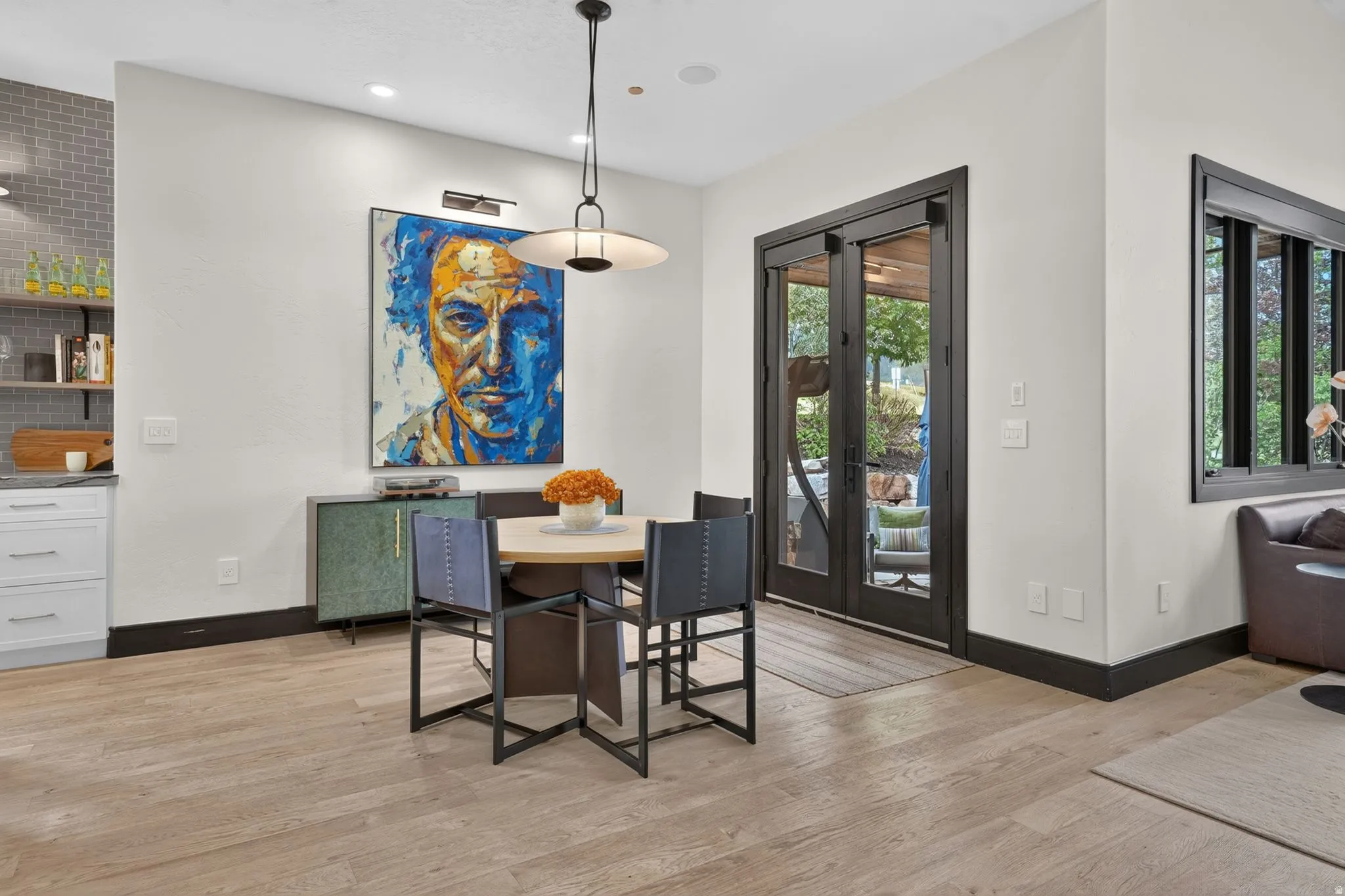 Light wood-finish flooring extending from the dining area, featuring a modern chandelier and dark-framed double doors leading to an outdoor space