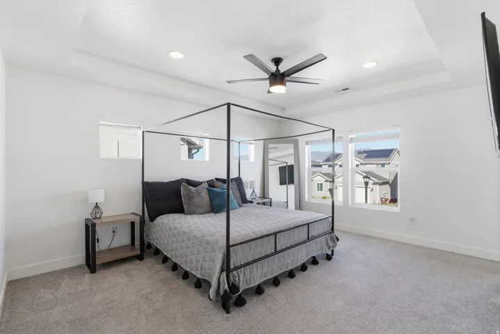 Bright bedroom featuring a tray ceiling with recessed lighting and a ceiling fan