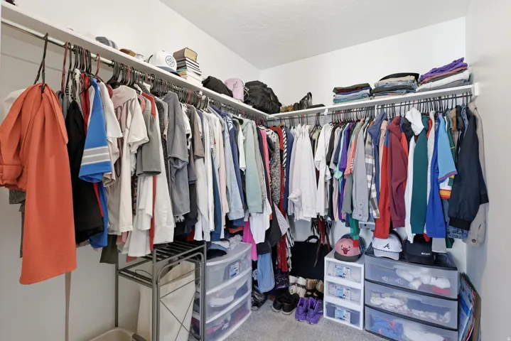 Walk-in closet featuring white walls, white shelving, and multiple hanging rods