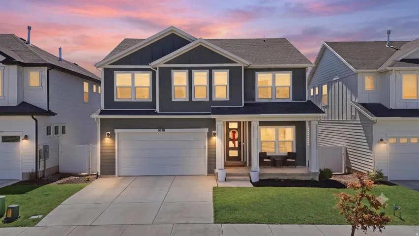 Two-story residence featuring a dark gray facade with white trim, a covered front porch with white pillars, a two-car garage, and a manicured front lawn