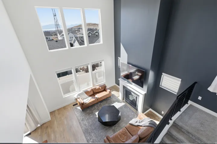Two-story living area featuring a fireplace with a white mantel, a television mounted above the fireplace, a black metal staircase railing, and wood-finish flooring