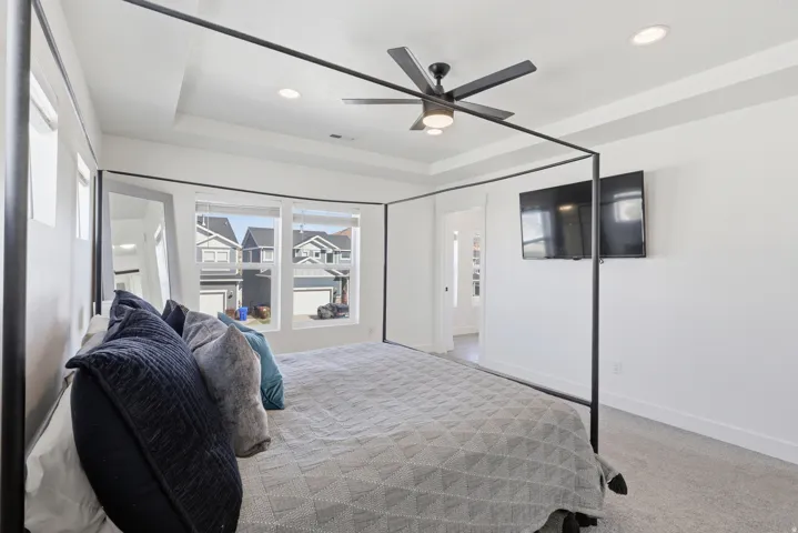 Spacious room featuring a tray ceiling with recessed lighting and a ceiling fan, light gray carpeting, and multiple windows providing ample natural light