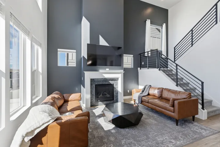 Two-story living area featuring a fireplace with stone surround and white mantel, a vaulted ceiling, multiple windows, and a staircase with black metal railings