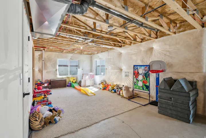 Unfinished basement space featuring exposed wooden ceiling joists and ductwork, multiple windows, and partial wall insulation