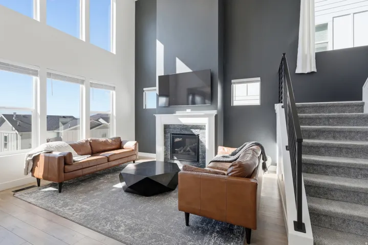 Living space featuring high ceilings, a fireplace with a white mantle and dark stone surround, wood-finish flooring, and multiple large windows