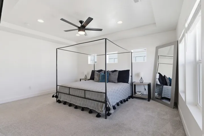 Recessed lighting illuminates a room featuring a tray ceiling, light neutral carpeting, and a ceiling fan