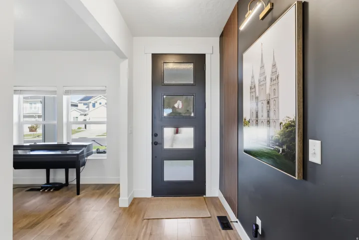 Entryway featuring a contemporary black door with three frosted glass panels, wood-finish flooring, white trim, and a dark accent wall