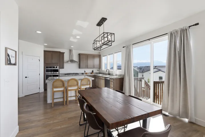Open-concept dining and kitchen space featuring wood-finish flooring, a contemporary linear chandelier, and sliding glass doors