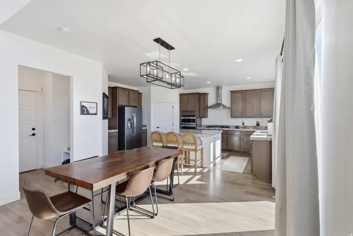 Open-concept kitchen and dining area featuring light wood-finish flooring, a kitchen island with seating, dark wood cabinetry, and stainless steel appliances
