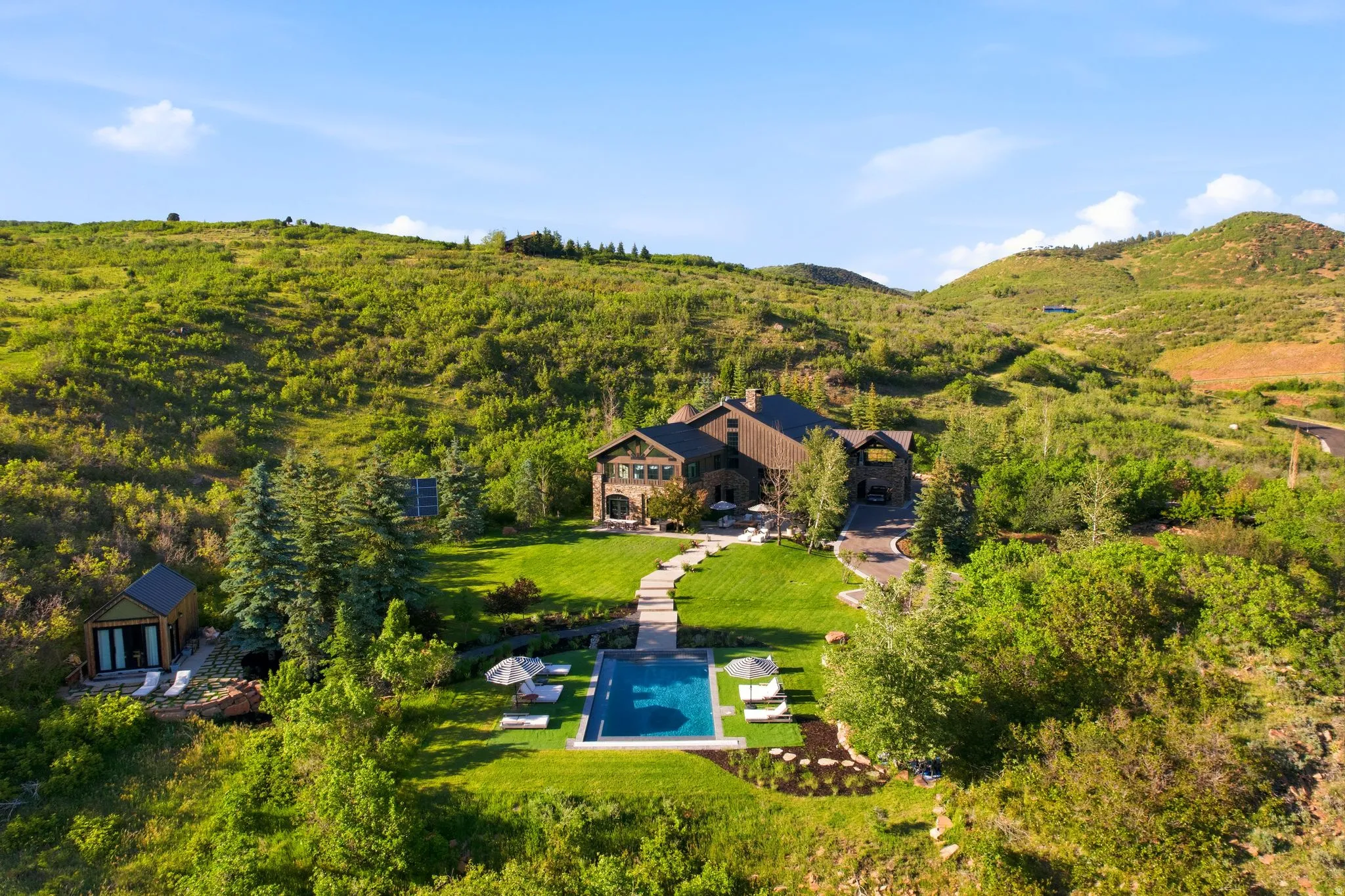 Stone and wood-clad residence with a rectangular swimming pool, expansive lawn, and mature landscaping