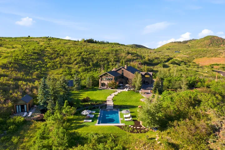 Stone and wood-clad residence with a rectangular swimming pool, expansive lawn, and mature landscaping