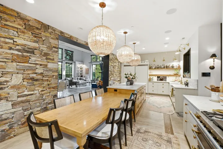 Open-concept dining and kitchen area featuring a stone accent wall, three spherical beaded pendant lights, a gas range with a substantial hood, and extensive cabinetry with gold-toned hardware