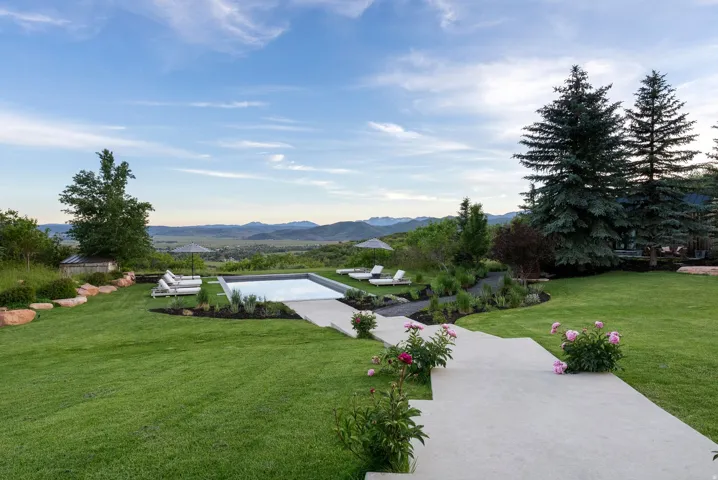 Spacious lawn with a rectangular swimming pool, concrete patio, and mature evergreen trees
