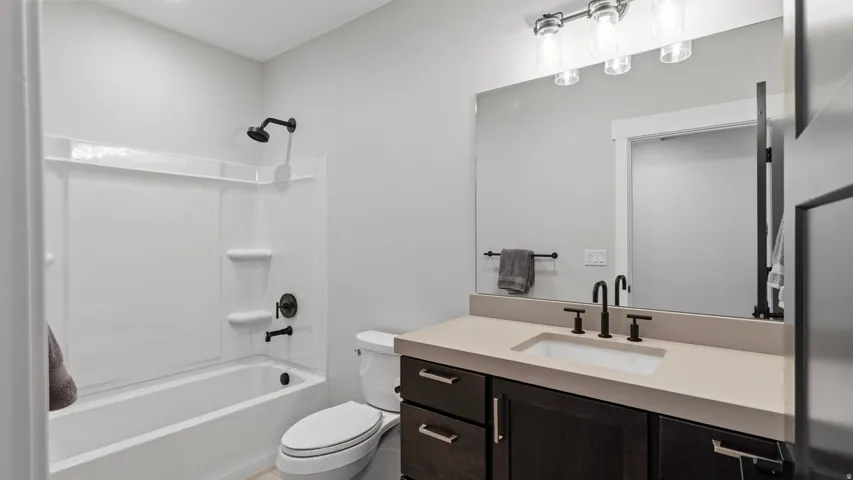 One of two lower level bathrooms, Bathroom #3 features a white tub/shower combination with matte black fixtures, a white toilet, and a vanity with a light-colored countertop and dark wood-finish cabinetry