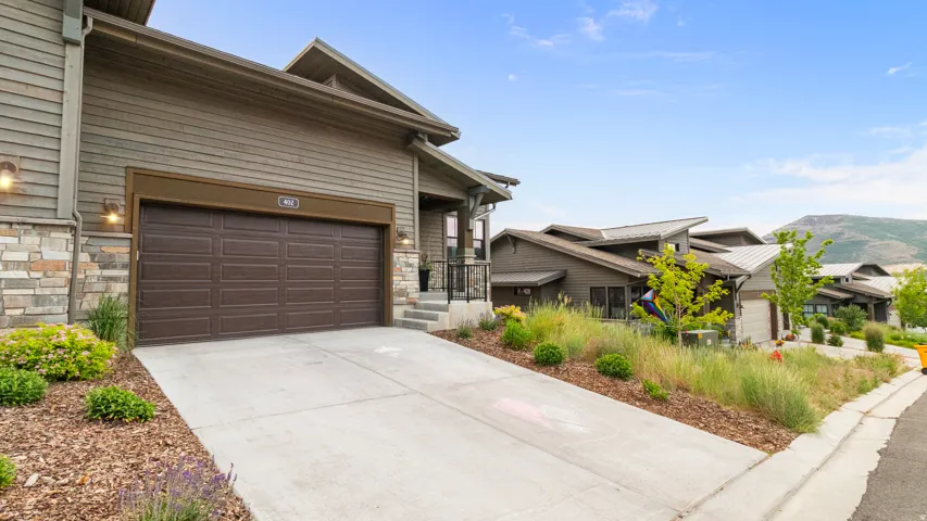 Exterior facade featuring horizontal siding, natural stone accents, a two-car garage, and integrated outdoor lighting fixtures