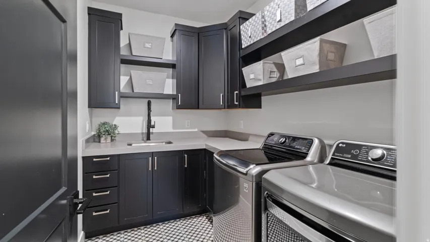 Main level laundry room featuring dark cabinetry, light countertops, a utility sink with a matte black faucet, and patterned floor tiling.  Plumbed for both gas and electric.