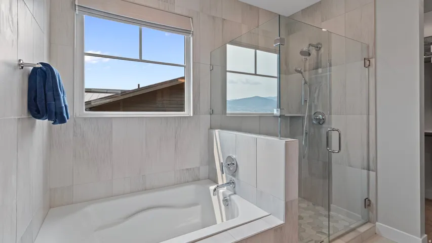 Primary suite's modern bathroom featuring a built-in tub, a glass-enclosed shower with a rainfall shower-head, and light-toned tile finishes