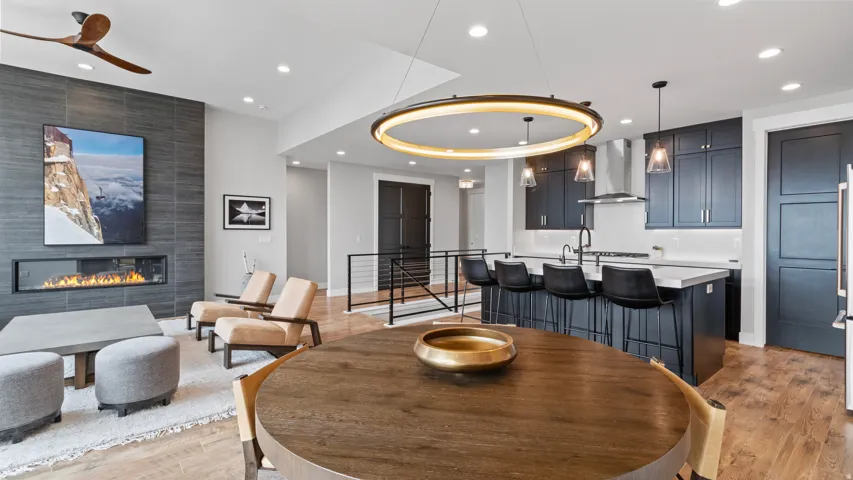 Open-concept living space featuring a linear fireplace with a dark tile surround, a built-in kitchen island with seating, dark cabinetry, pendant lighting, and wood-finish flooring